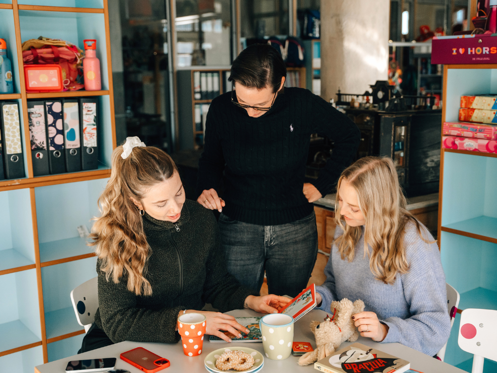 Drei junge Frauen sind in einem Büro und sehen sich gemeinsam ein Buch an