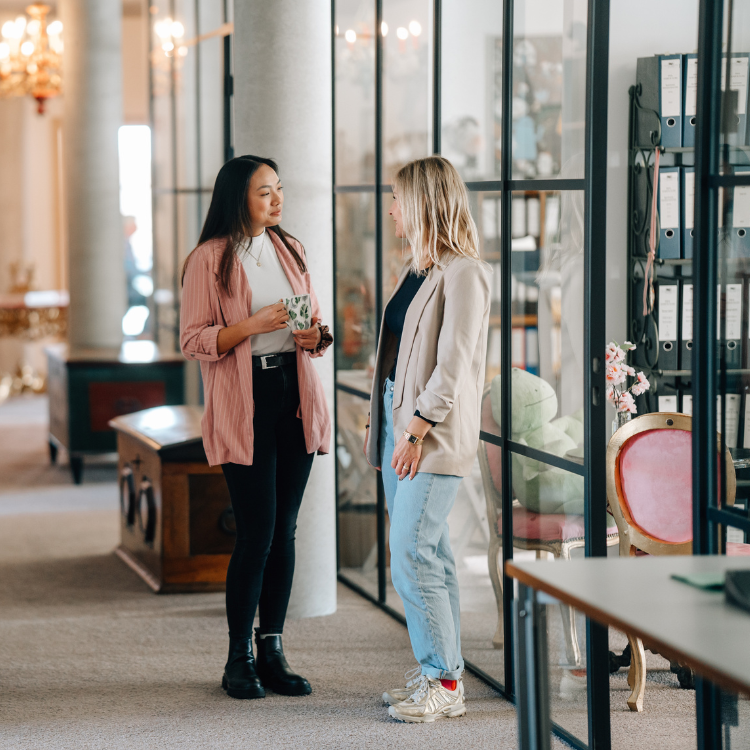 Zwei junge Frauen im Business-Outfit unterhalten sich im Flur