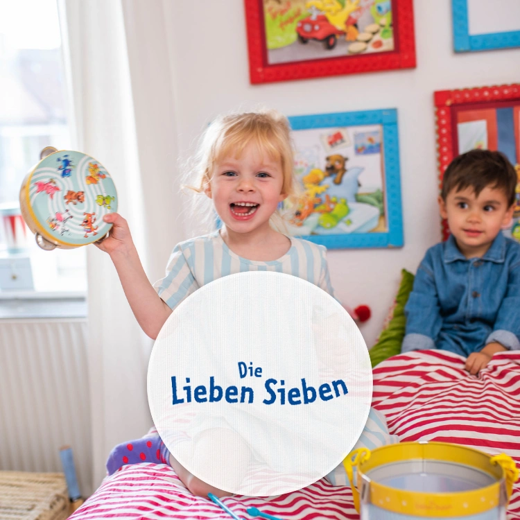 Ein Mädchen hält lachend einen Ball hoch, während ein Junge neben ihr sitzt und zuschaut