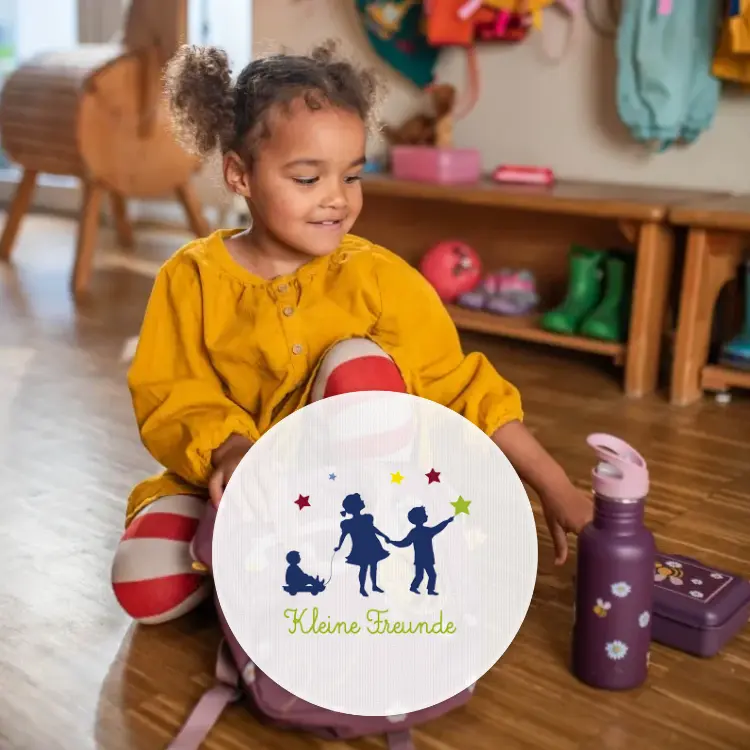 Mädchen im Kindergartenalter greift zu einer lila Trinkflasche, die neben einer liila Brotdose liegt